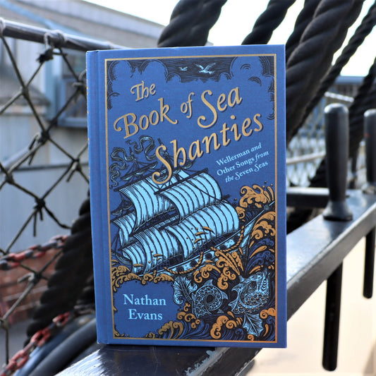 The image shows a book titled 'The Book of Sea Shanties' by Nathan Evans, placed on a surface with nautical-themed decorations in the background.
