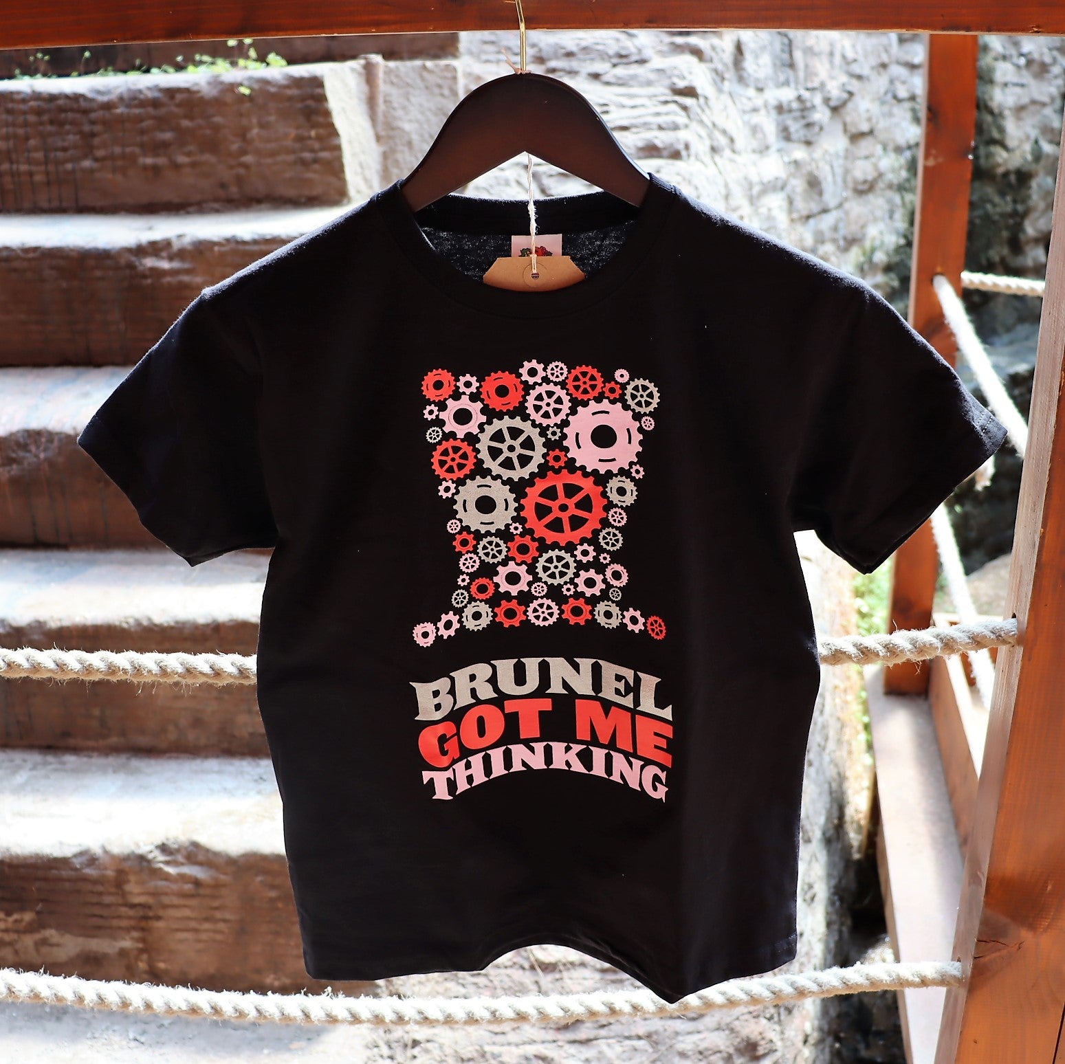 A black kids t-shirt with a graphic print of mechanical gears and the text 'BRUNEL GOT ME THINKING' on the front.