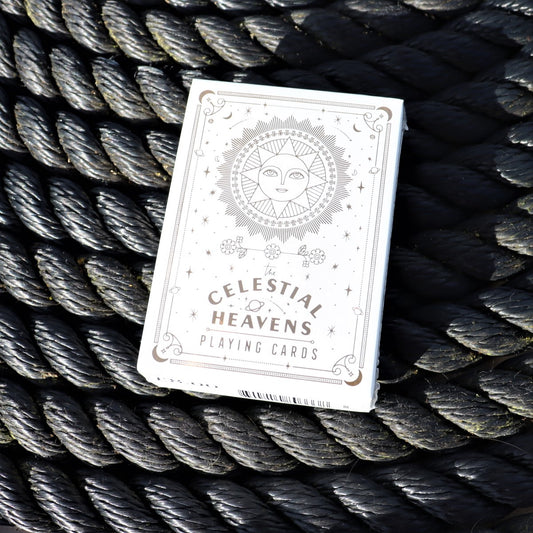 A deck of playing cards with gold foil stamping and celestial themed designs, placed on a woven surface.