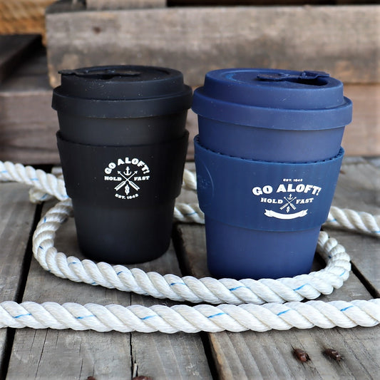 Two travel mugs, one black and one blue, with 'GO ALOFT' text on them, placed on a wooden surface with a white rope in the background.