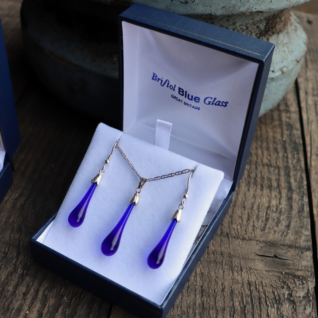 Jewelry set with blue teardrop pendants in a 'Bristol Blue Glass' box on a wooden surface.