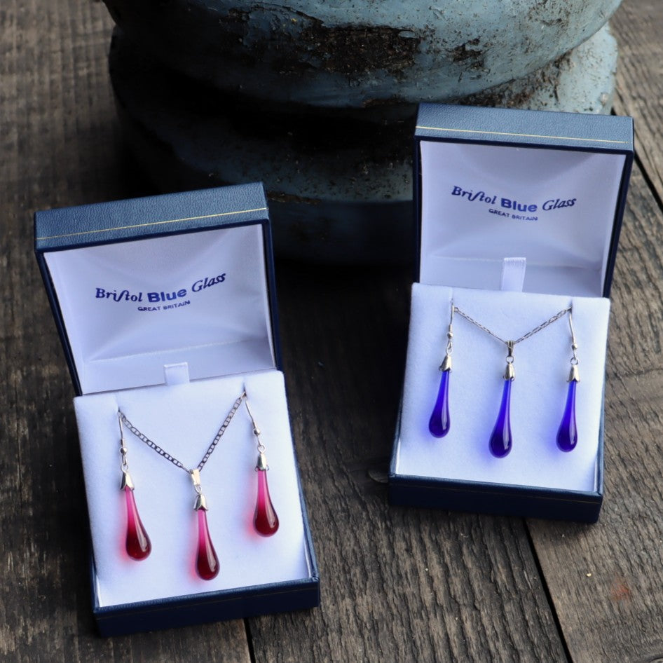 Jewelry set with teardrop-shaped pendants in open boxes labeled 'Bristol Blue Glass' on a wooden surface.