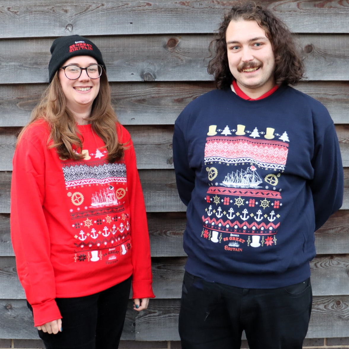 Two adults, one female and one male, wearing colorful Christmas-themed sweaters featuring nautical designs and the SS Great Britain.