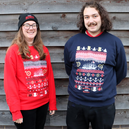 Two adults, one female and one male, wearing colorful Christmas-themed sweaters featuring nautical designs and the SS Great Britain.