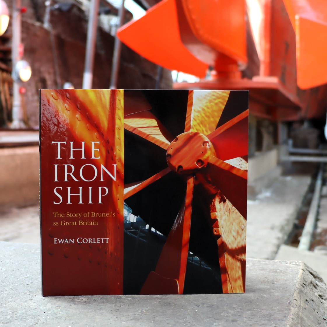 A book titled 'The Iron Ship' displayed in front of a historical maritime backdrop, featuring color illustrations related to the SS Great Britain.