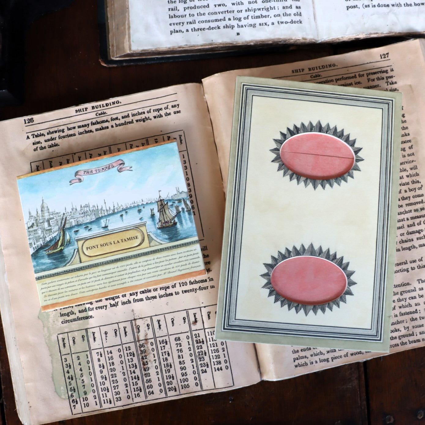 A hand-cut peep show replica displayed on an open book, illustrating a historical scene with red view holes.