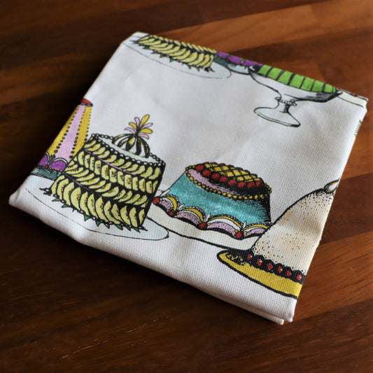 A multicolored tea towel with illustrations of various Victorian desserts.